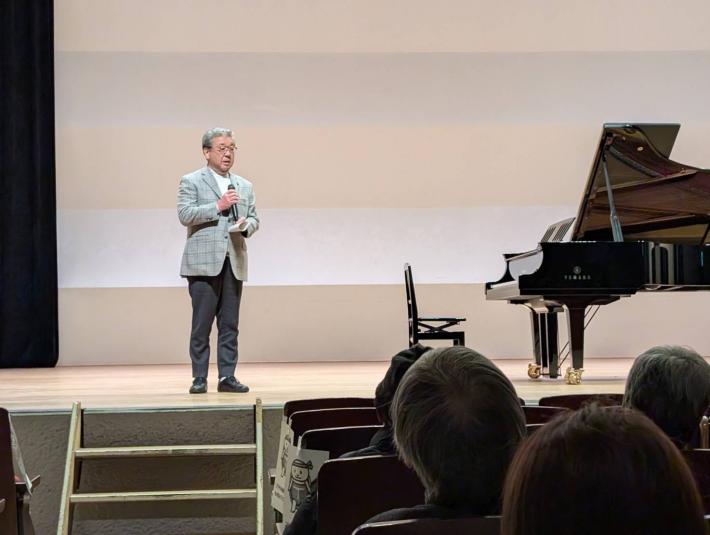 ピアノの横に立ちあいさつをする男性