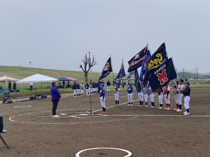 野球場で旗を持つ選手たちとその前に立つ男性