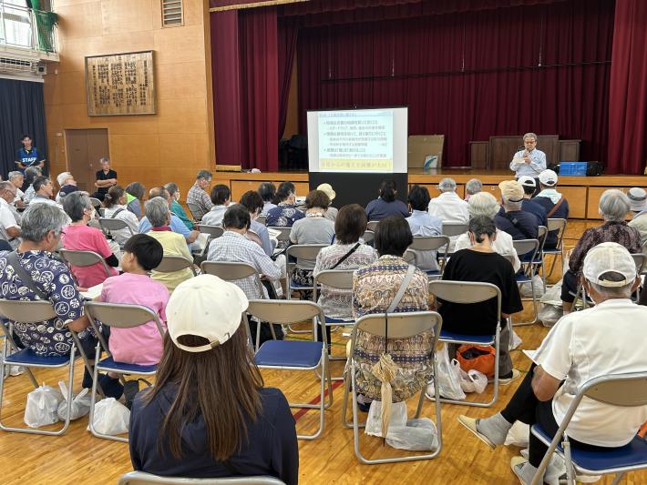 体育館で話をする男性とそれを聴く人たち