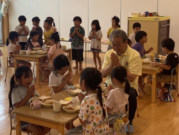 給食の前で手を合わせる子供と男性