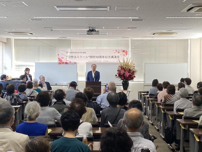 椅子に座っている人たちとその前で話をする男性