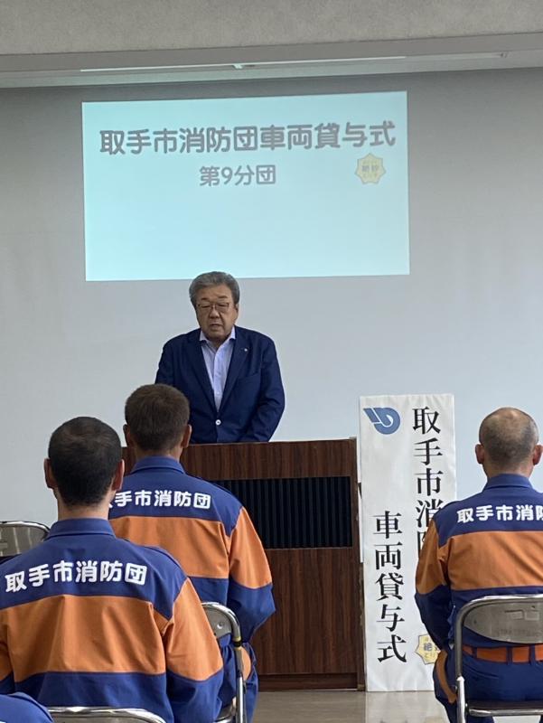 消防車両貸与式と書かれた幕の横に立ち話をする男性