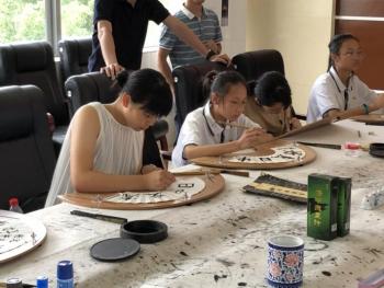 団員が中国人学生と一緒に扇の紙に筆で字を書いている様子