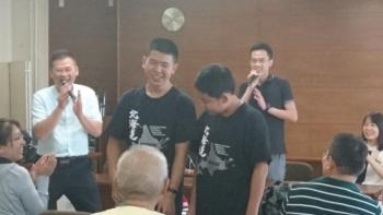 ペアルックをきた男子学生が2人笑顔で並び、その後ろにコメントを行っている桂林市側の職員がいる。