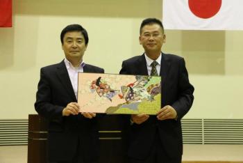 取手市から贈呈した記念品を、桂林市団長と市長が同時に手に持ち、記念撮影に応じている様子。