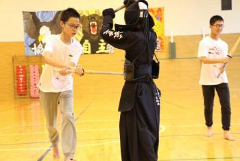 部活動体験で防具をつけた日本人生徒と、竹刀を手にした中国人男子学生が「胴」を打ち込んでいる画像。