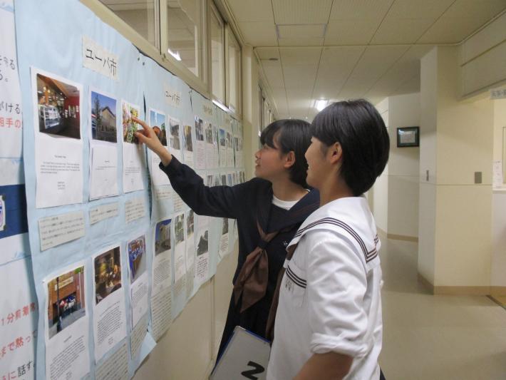 ユーバ市の学生による作品を指さしながら鑑賞する戸頭（とがしら）中学校の女子中学生2名