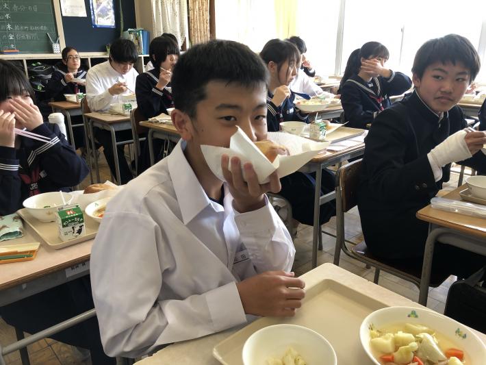 紙に包まれたパンを口を隠しながら食べる男子生徒