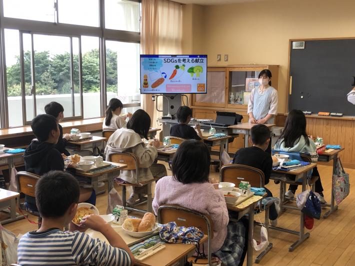 大型掲示装置に映された画像を見ながら給食を食べる子どもたち