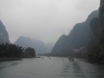 霧がかった山岳の間を流れる大きな川とそれを下る船