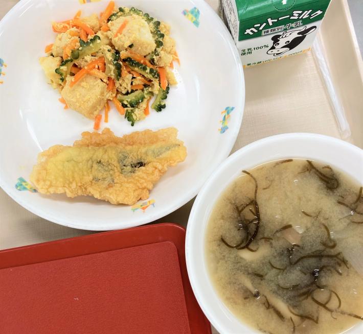 お盆にのせられた給食。お椀にはもずくが入った味噌汁。お皿にはゴーヤーと豚肉と卵の炒め物、天ぷら。