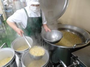 大型のおたまを使い味噌汁を食缶に入れる様子