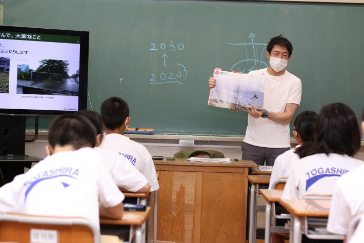 杉浦先生が参考書を手元に持って地球温暖化や気候変動による影響を参加している生徒を説明している