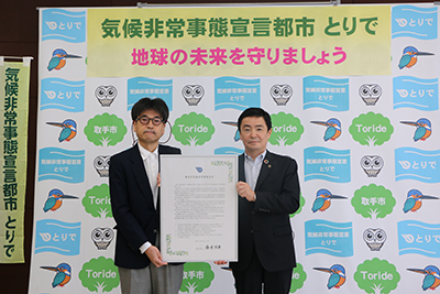 気候非常事態宣言書を掲げる藤井信吾市長（右）と市環境審議会の氷鉋揚四郎会長（左）の写真です。