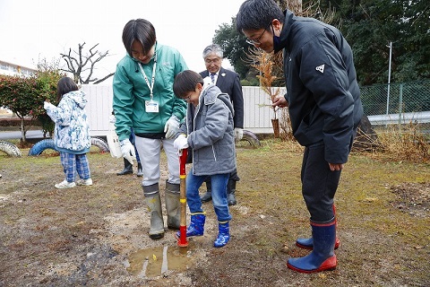 児童と保護者が植樹会の関係者と共にスギの苗を植えている様子。