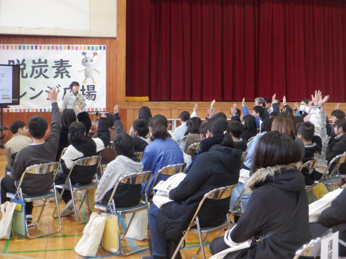 県南農林事務所の職員が児童や保護者等に森林について説明し写真。職員が参加者にクイズを出し、参加者が手を挙げてクイズに答えている。