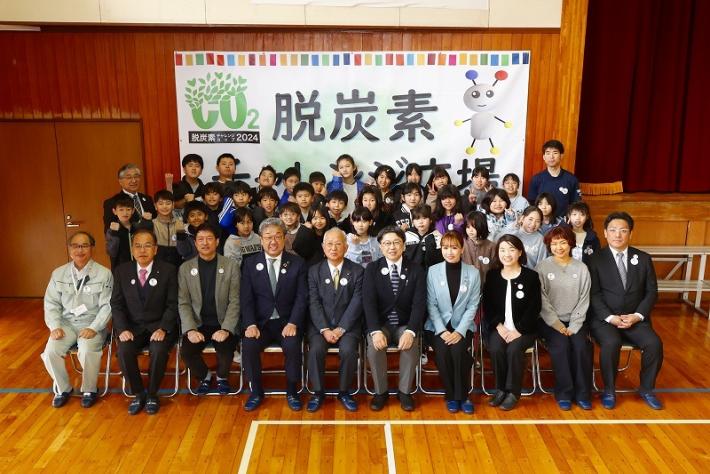 植樹会の関係者たちが記念撮影を行っている写真。脱炭素チャレンジカップの垂れ幕を背景に児童や関係者が整列している