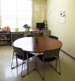 青少年センター相談室の中の写真。花の置かれた丸テーブルに椅子が4脚置かれている。