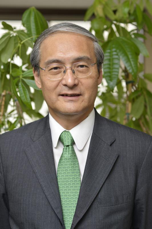 久保田先生画像。スーツ・グリーンのネクタイでめがねをかけた男性が微笑んでいる胸上写真。