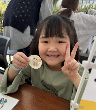 完成した缶バッジの紙を見せてピースしている