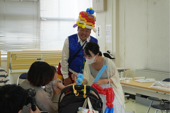 さくらまやさんと頭にバルーンを乗せた男性がグッズを会員に渡している様子