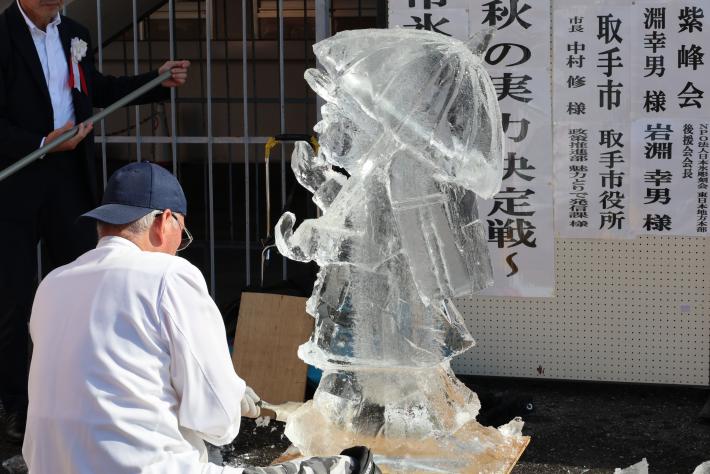 男性が氷彫刻で傘を差した子供を作っている様子
