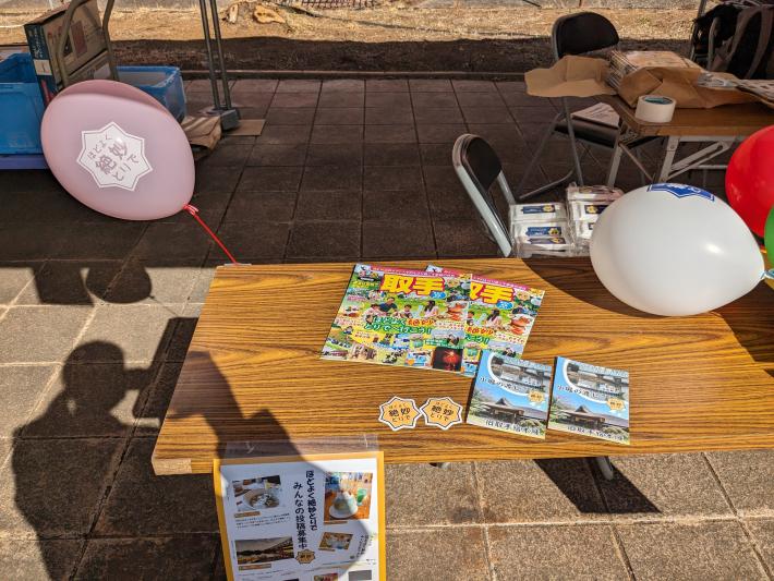 テーブルにピンクの風船や、るるぶ、ポストカード、ロゴのステッカー等がおいてある。