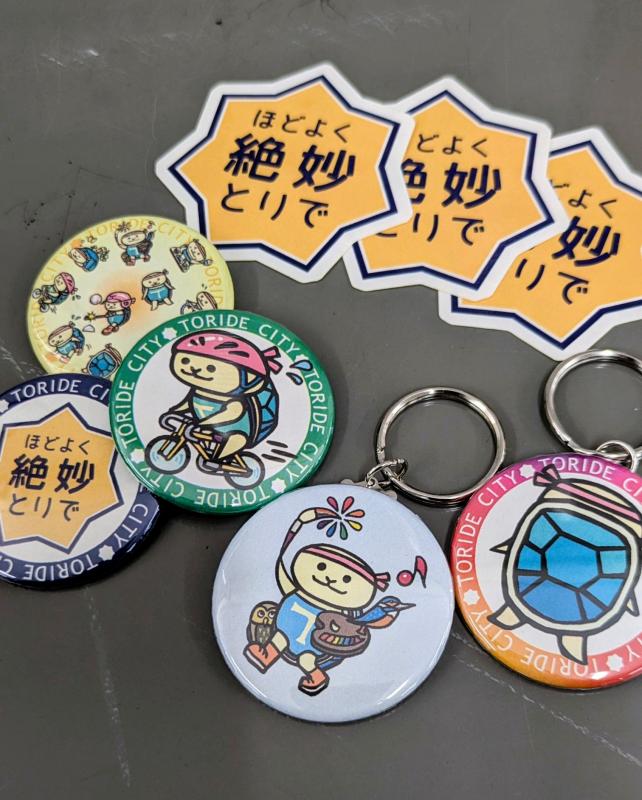 YouTubeとInstagram登録者限定ガチャガチャでの景品写真。とりかめくんの缶バッジやステッカー、キーホルダー。