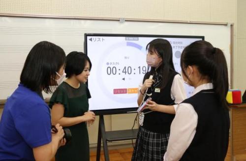 若い女性たちにスマートフォンの画面を見せて何かを話す学生の様子