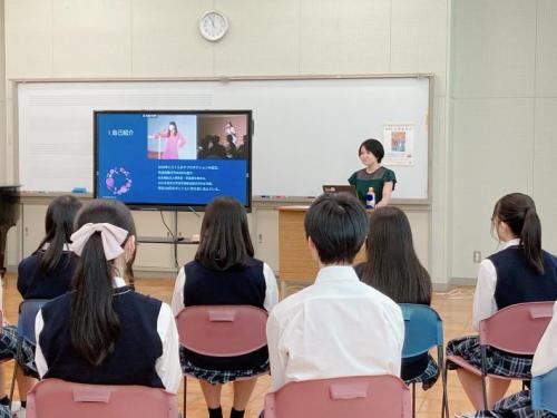 講義室前のモニターに資料を写し説明している女性とそれを聞いている学生の写真
