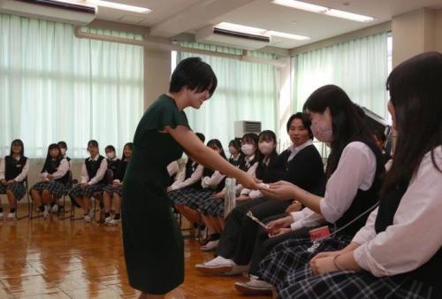並んで着席している学生に何かを渡している若い女性の写真