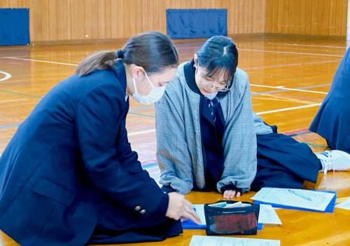 2人の女子生徒が床においた紙を見て何かを考え、話している様子