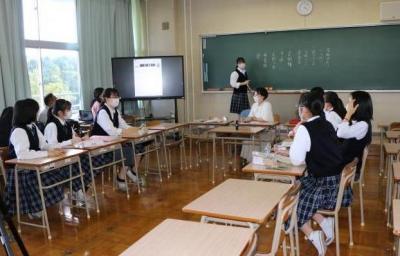 教室前方の黒板に生徒がいくつかの項目を書き出しながら振り向いて後ろにいる生徒たちと話している写真。