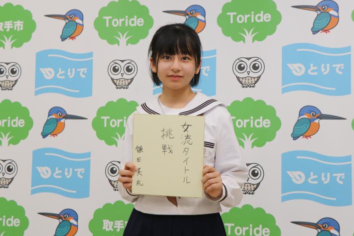 「女流タイトルに挑戦」という色紙を手に笑顔を浮かべる女子中学生