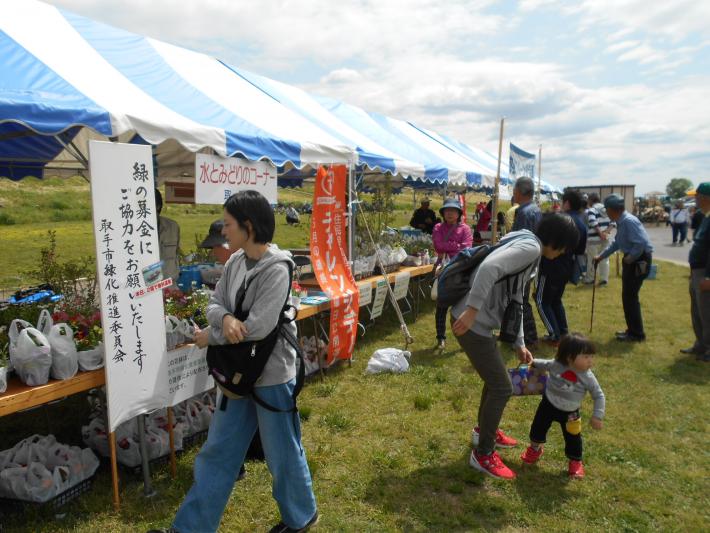 緑化イベント（こども天国）の様子。青いテントが立っており、その前を人が歩いている。