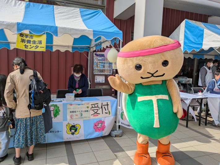 とりかめキャラクター着ぐるみがテントの前で手を振っている