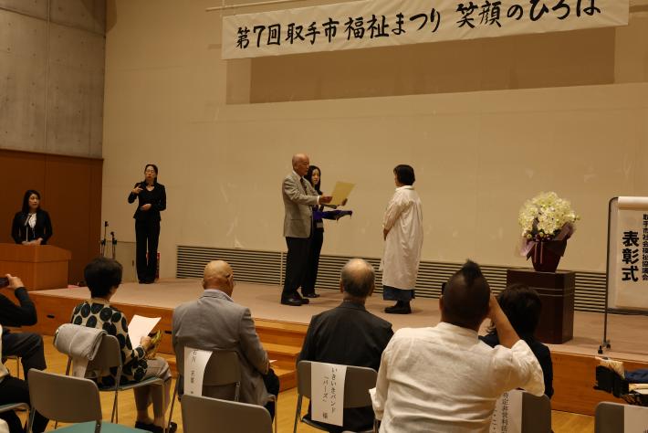 賞状を持った授与者の男性と受領者の女性がステージ上で立っている