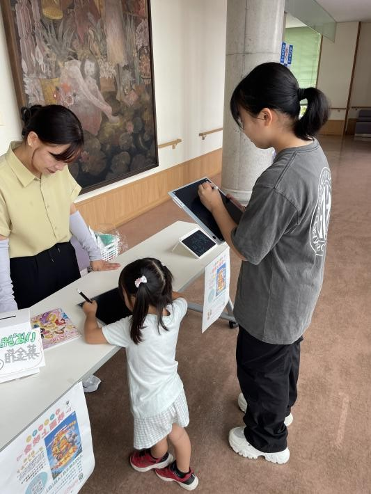 会場受付にて女性と子どもが受付用紙に記入している。