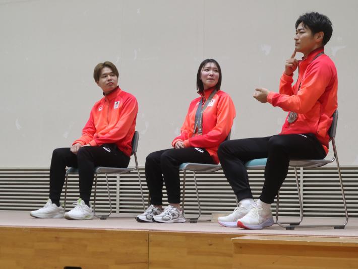 デフスポーツ選手男女3名が壇上で手話で受け答えをしている。