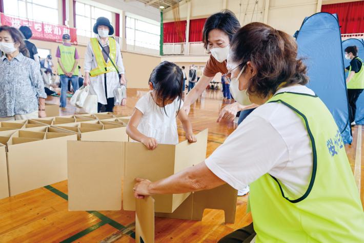 地域の大人が子ども達に段ボールベッドの作り方を教えている様子