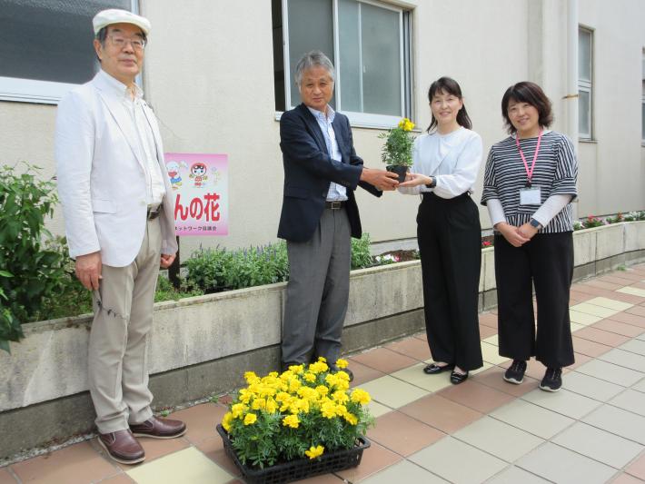 学校の前で男性二人が女性二人に花苗を手渡している様子