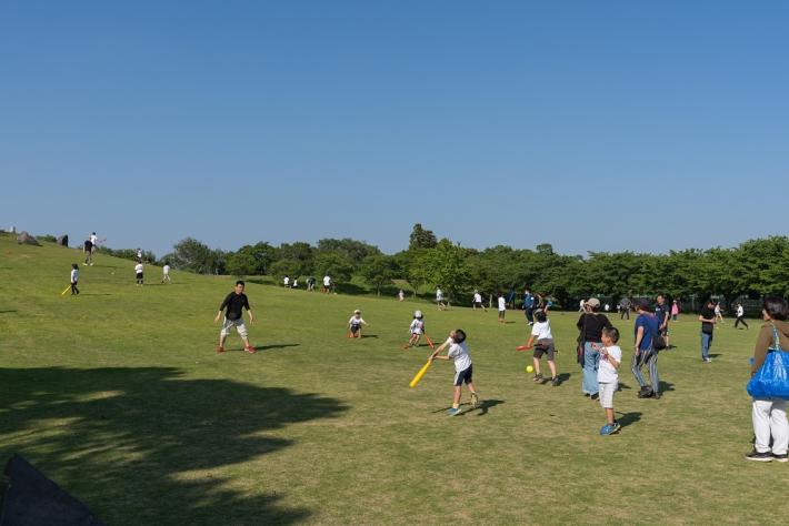 子どもたちがバットやボールを使って広場で遊んでいる