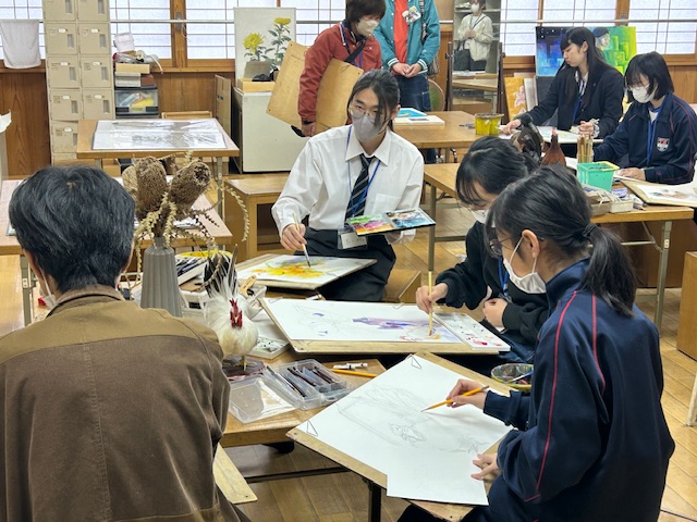 小中学生が机の上に置かれたものを見ながら絵を描いている。